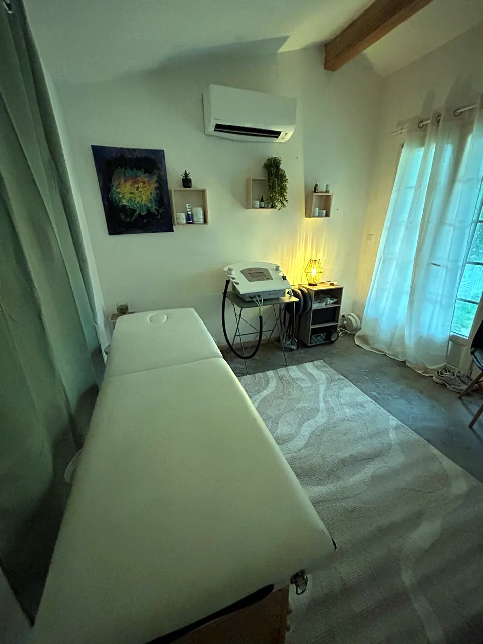 La salle de soins vue depuis la table : l’appareil de cryothérapie, la lampe et la porte-fenêtre
